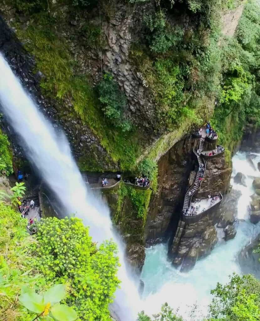 Turistas contemplando una cascada tropical desde las escaleras del acantilado.