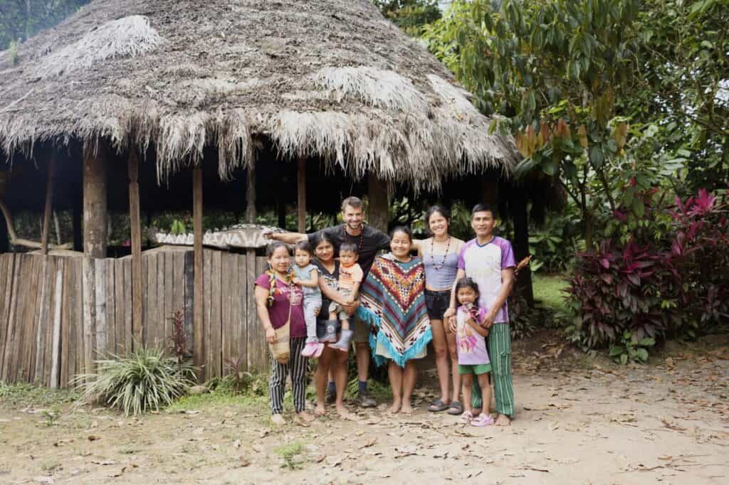 Grupo sonriendo fuera de una cabaña tradicional con techo de paja.