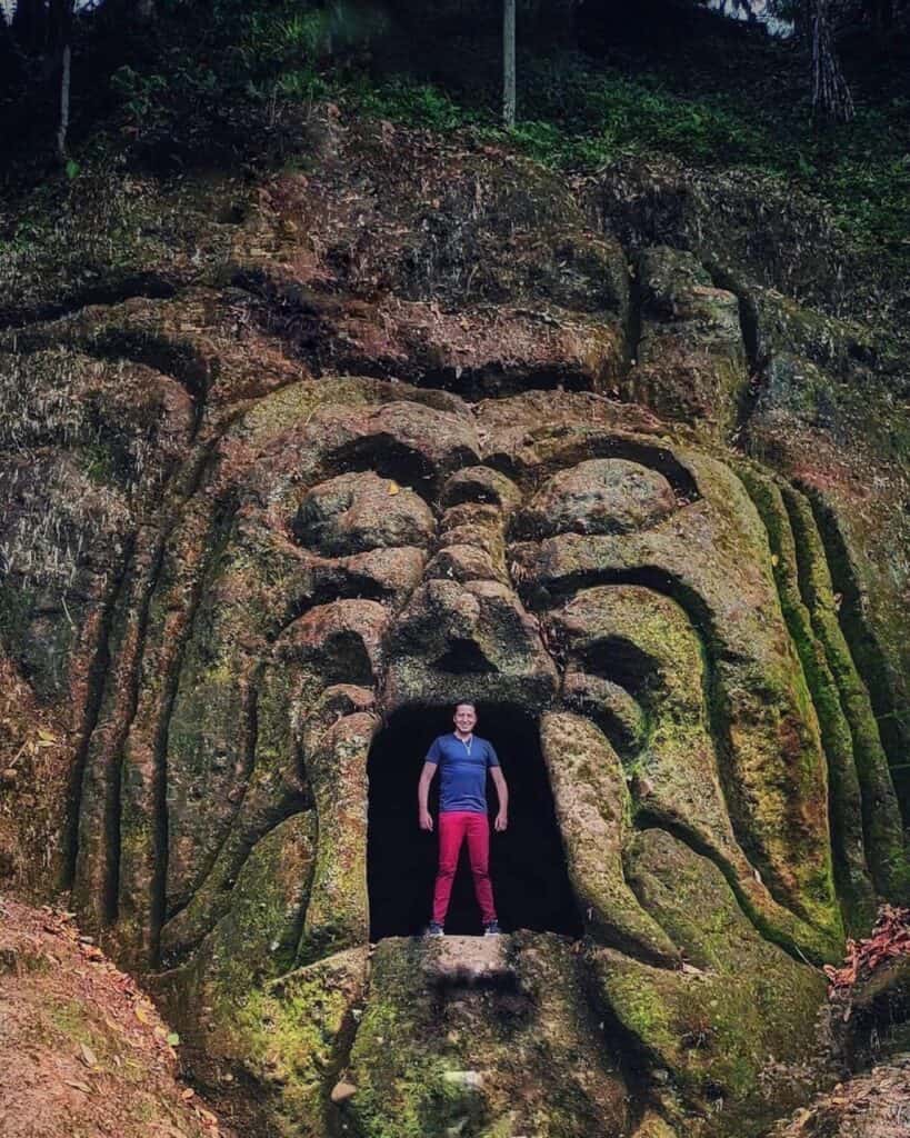 Persona de pie en la entrada de una escultura gigante con forma de rostro de piedra.