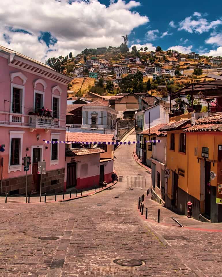 Colorful street leading to hillside statue in Quito