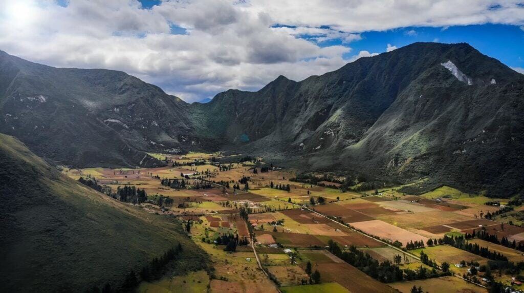 Green valley surrounded by tall mountains under clouds