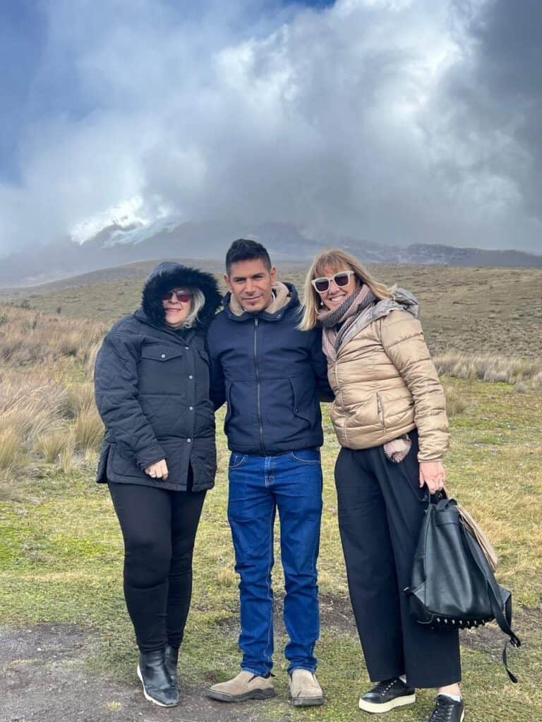 Three people posing outdoors near cloudy mountain.